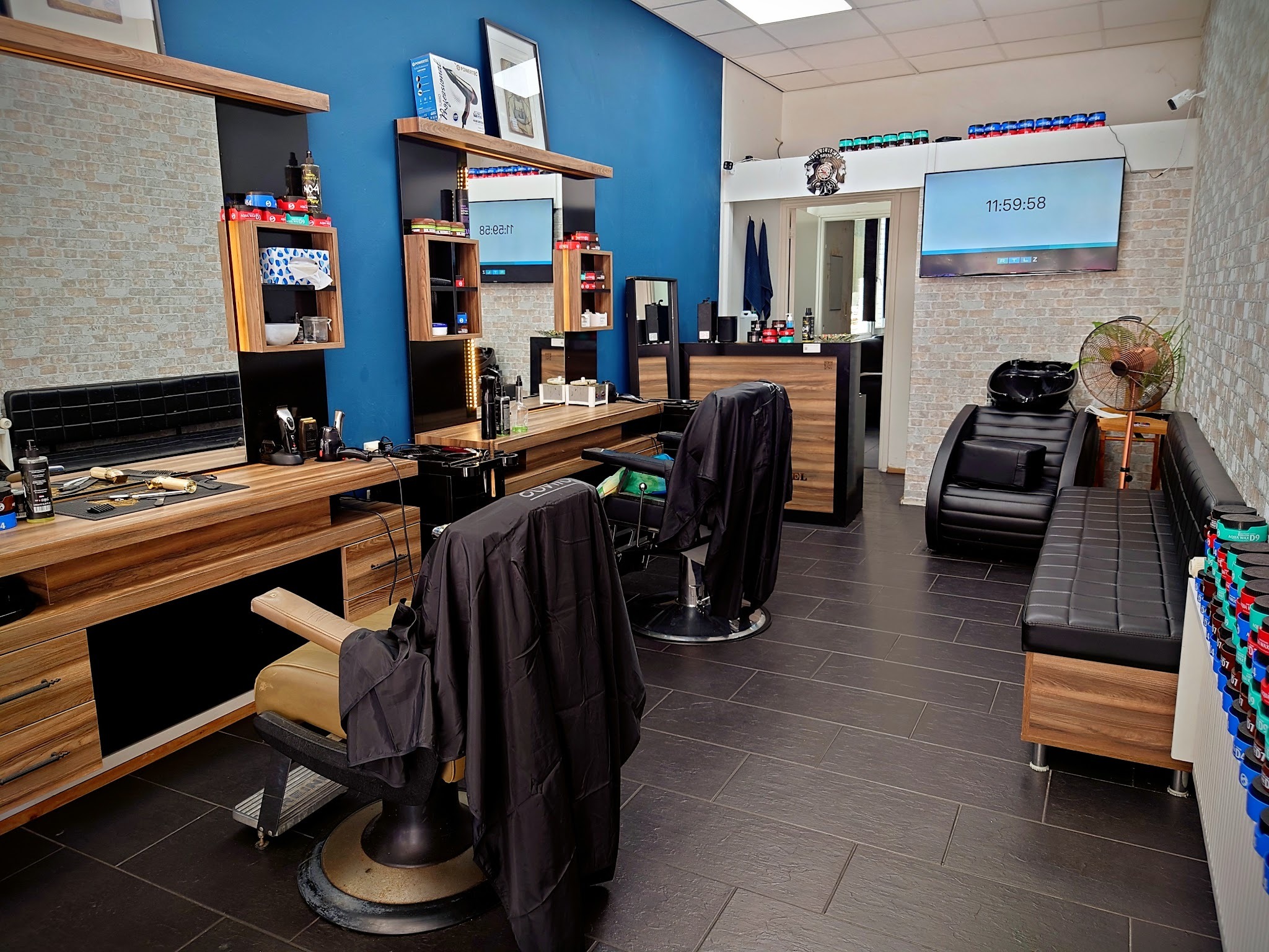 De zaak van Barber Labs: blauwe wand, houten kapstations met stoelen, wasbak en televisie