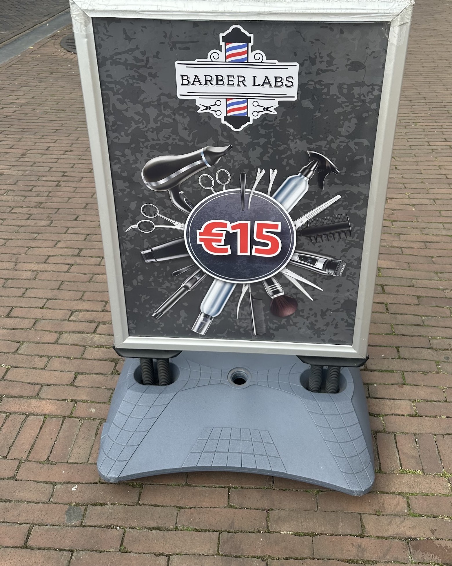 Het stoepbord van Barber Labs op de Hoofdstraat: logo, kappersgereedschap en de prijs € 15